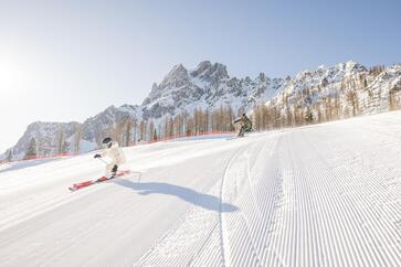 Ein Mann und eine Frau fahren mit Skiern eine Piste hinab