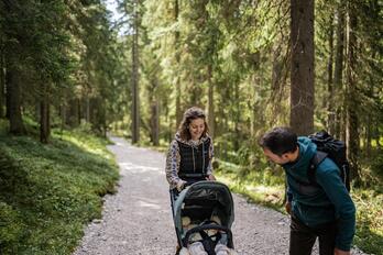 Ein Mann und eine Frau spazieren mit dem Kinderwagen durch den Wald