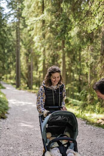 Ein Mann und eine Frau spazieren mit dem Kinderwagen durch den Wald