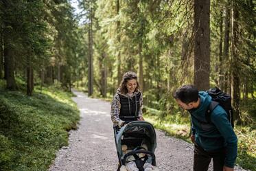Ein Mann und eine Frau spazieren mit dem Kinderwagen durch den Wald