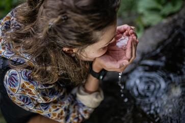 Eine Frau trinkt Wasser aus einem Bach