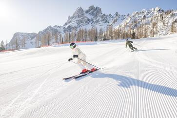 Ein Mann und eine Frau fahren mit Skiern eine Piste hinab