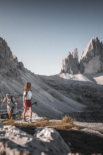 Ein Mann und eine Frau wandern in den Dolomiten, im Hintergrund erheben sich die Drei Zinnen
