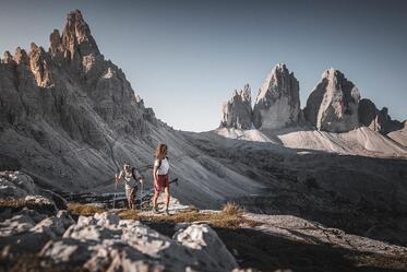Ein Mann und eine Frau wandern in den Dolomiten, im Hintergrund erheben sich die Drei Zinnen