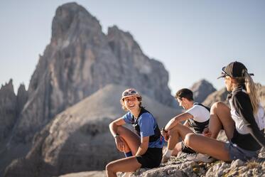 Drei Bergläufer sitzen in steinigem Gelände und schauen auf die massive Berglandschaft.