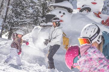 Ein Mann spielt mit drei Kindern im Schnee