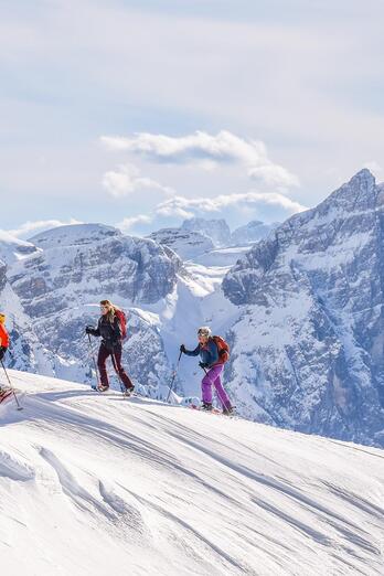 Drei Personen beim Schneeschuhwandern umgeben von den Dolomiten