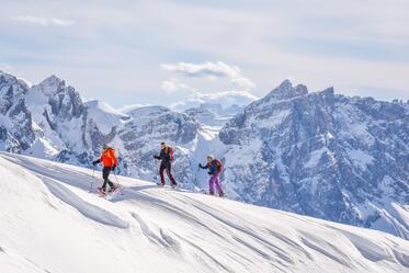 Drei Personen beim Schneeschuhwandern umgeben von den Dolomiten