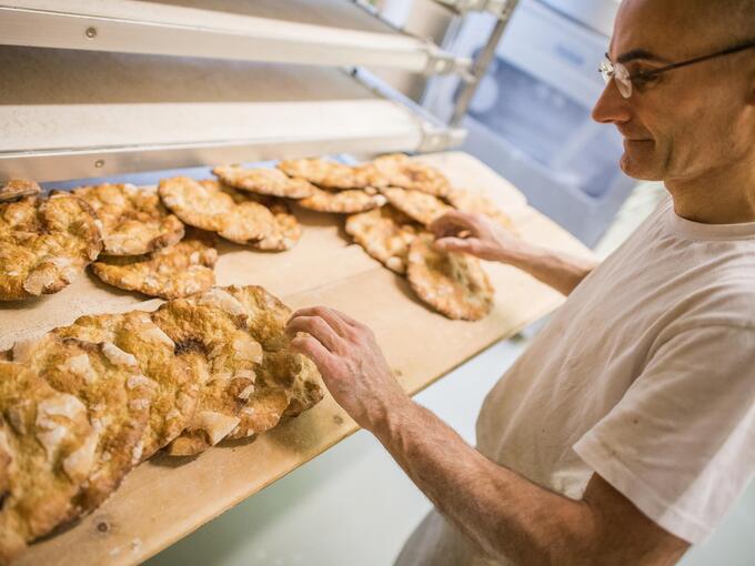 Ein Mann steht in einer Backstube und kontrolliert frisch gebackenes Schüttelbrot auf einem Regal