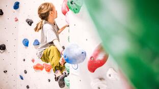 Ein Kind klettert an einer Boulderwand in einer Kletterhalle