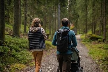 Ein Mann und eine Frau spazieren mit dem Kinderwagen durch den Wald