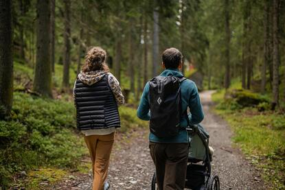Ein Mann und eine Frau spazieren mit dem Kinderwagen durch den Wald