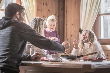 Eine Familie mit zwei Kindern sitzt an einem Tisch und genießt Südtiroler Gerichte